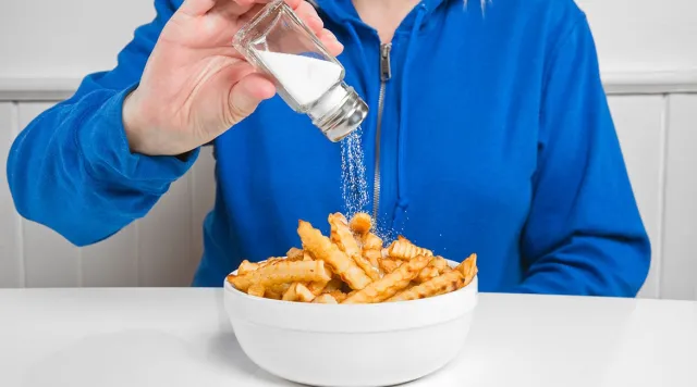 Person salting a bowl of french fries